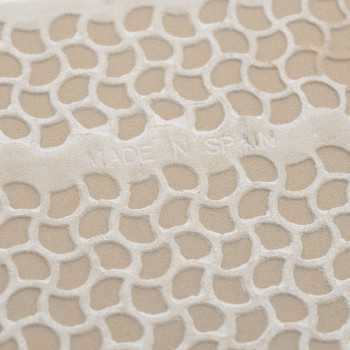 Azulejo texturizado con diseño de panal en relieve, que muestra el texto `MADE IN SPAIN`. La superficie tiene un fondo beige.