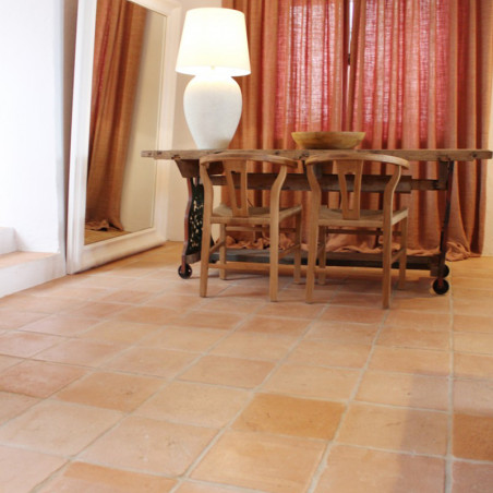 Terracotta tiles form a rustic floor, supporting wooden furniture and a lamp in a warmly lit room with curtains.