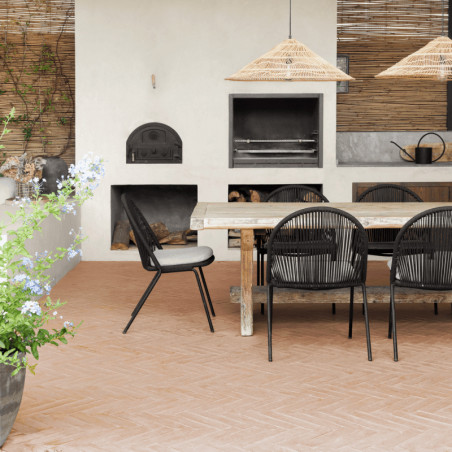 Terrakottafliesen bedecken eine Terrasse, auf der unter Strohlampen ein Ess-Set aus Holz und an weißen Wänden ein Lehmofen steht