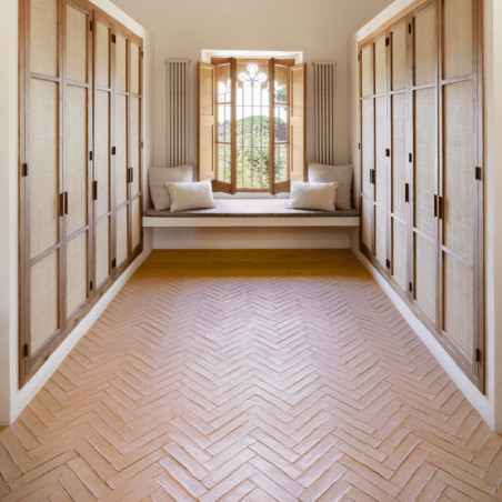 Terracotta tile floor arranged in a herringbone pattern, flanked by wooden cabinets, leads to a sunlit window bench.