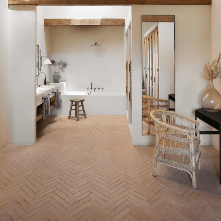 Terracotta tiles cover the floor, arranged in a herringbone pattern. they enhance a rustic bathroom with light decor.