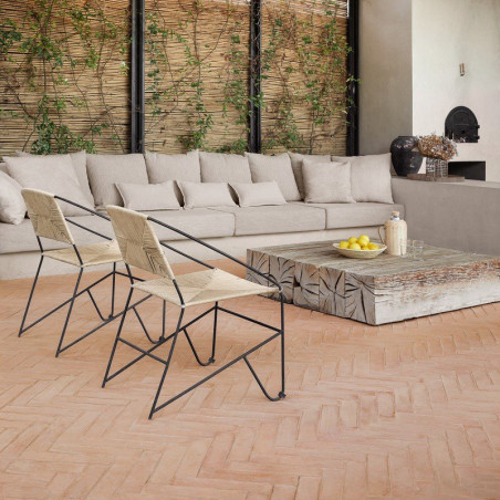 De terracotta tegelvloer ondersteunt zwart metalen stoelen en een stenen tafel, in een gezellige woonruimte met beige meubels.