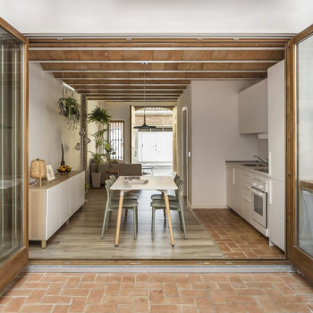 Ladrilhos de terracota formam um teto arqueado acima de uma cozinha moderna com armários brancos, mesa de jantar e área de estar