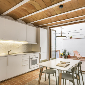 Des carreaux de terre cuite forment un plafond voûté au-dessus d'une cuisine moderne avec des armoires blanches, une table à man