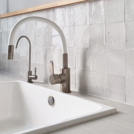 Gebogen witte kraan boven witte gootsteen, omgeven door getextureerde witte terracotta tegels op een moderne keukenachterwand. Gebogen witte kraan boven witte gootsteen, omgeven door getextureerde witte terracotta tegels op een moderne keukenachterwand.