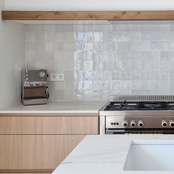 Ladrilhos de terracota brancos brilhantes formam um backsplash acima de um fogão moderno em uma cozinha elegante e minimalista.