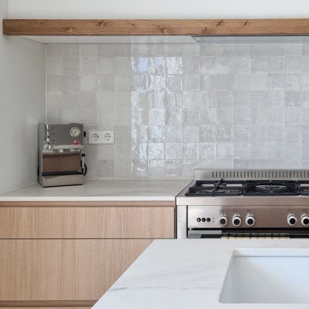 Ladrilhos de terracota brancos brilhantes formam um backsplash acima de um fogão moderno em uma cozinha elegante e minimalista.