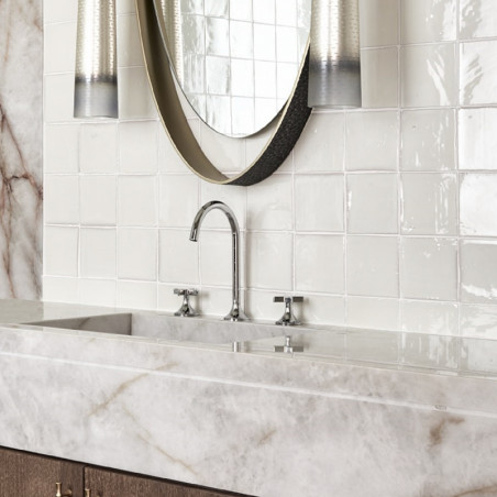 Los azulejos de terracota blanca se alinean en la pared del baño y reflejan la luz alrededor de una encimera de mármol con un gr Los azulejos de terracota blanca se alinean en la pared del baño y reflejan la luz alrededor de una encimera de mármol con un gr