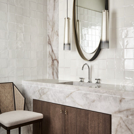 Des carreaux de terre cuite blanche recouvrent un mur de salle de bain, réfléchissant la lumière. lavabo en marbre en dessous, f