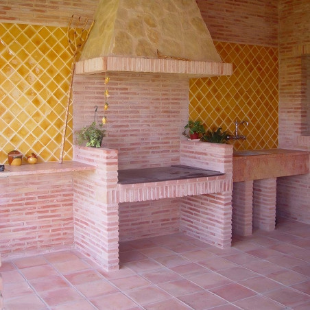 Des carreaux de terre cuite recouvrent un espace barbecue extérieur rustique, avec des murs à motifs de losanges jaunes, un four