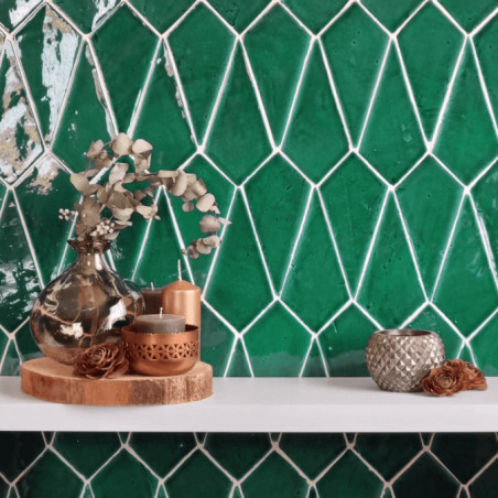 Green terracotta tiles form a geometric pattern. decorative vases and candles rest on a white shelf in front. Green terracotta tiles form a geometric pattern. decorative vases and candles rest on a white shelf in front.