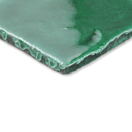 Carreau en terre cuite vert brillant, incliné dans la lumière naturelle, soulignant ses bords lisses et incurvés et sa surface b