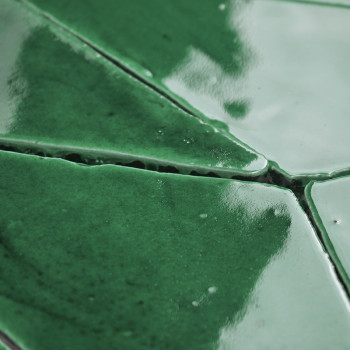 Green terracotta tiles, glossy and reflective, fit closely together, creating a seamless, geometric pattern within a tiled surfa