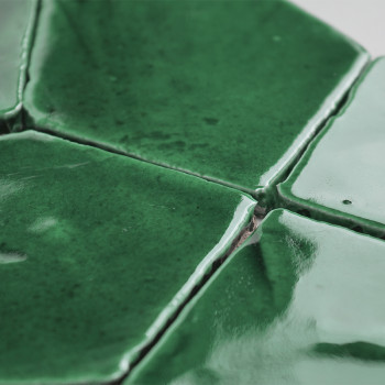 Green terracotta tiles, joined and glossy, form a textured pattern, capturing light in a close-up indoor setting.