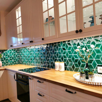 Green hexagonal tiles form a geometric backsplash, complementing wooden countertops in a bright, modern kitchen with white cabin