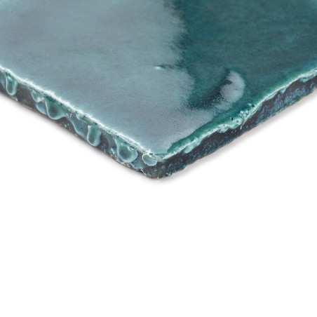 Een geglazuurde, groene terracotta tegel met een druipende textuur. rustend op een witte achtergrond, waarbij het glanzende oppe