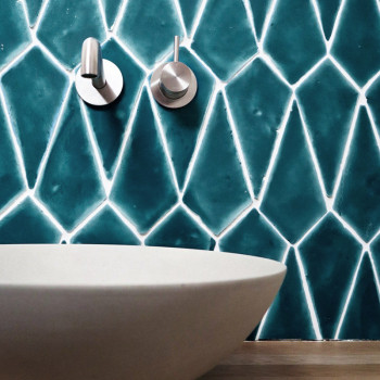 Des carreaux géométriques bleus en terre cuite recouvrent le mur d'une salle de bains au-dessus d'un lavabo blanc moderne, avec 