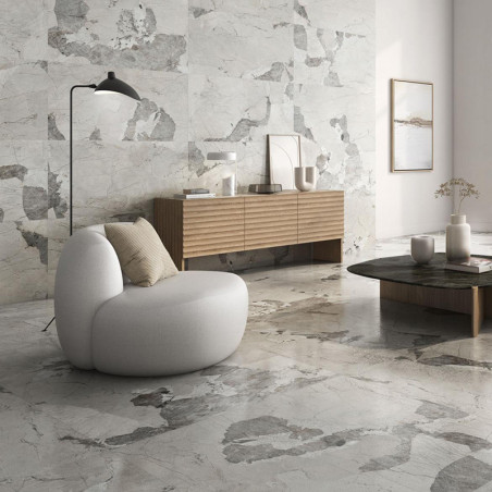 Een ronde grijze stoel staat op een marmeren vloer in een moderne woonkamer. Vlakbij staat een houten dressoir met decoratieve v