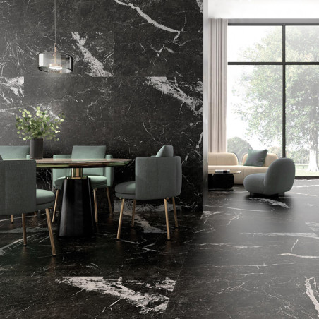 Un coin repas avec une table en verre et des chaises vertes repose sur un sol en marbre noir. A proximité, un coin salon cosy do