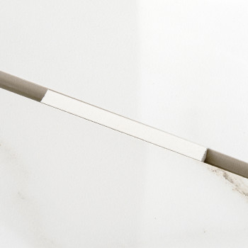 A rectangular, light-colored tile rests diagonally against a plain white background, exhibiting subtle gray veining and a clean,