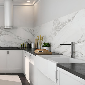 Een aanrecht is voorzien van witte kasten en een grijs aanrechtblad, met een grote gootsteen en moderne kraan, afgezet tegen ach