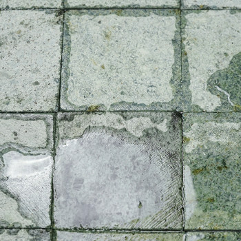 Natte vierkante stenen tegels met onregelmatige patronen, die licht reflecteren, gerangschikt in rijen waardoor een gestructuree