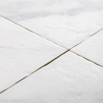 Quatre carreaux carrés blancs se rejoignent aux coins, formant un motif en « X », avec une légère texture visible, suggérant une