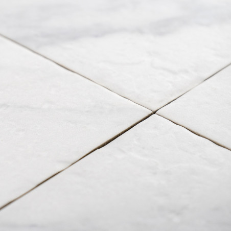Quatre carreaux carrés blancs se rejoignent aux coins, formant un motif en « X », avec une légère texture visible, suggérant une