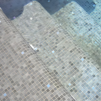 As telhas de vidro formam degraus submersos na água, criando um padrão cintilante sob a água da piscina transparente e em movime