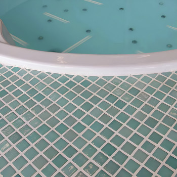 Una bañera de hidromasaje circular reposa, llena de agua, sobre un piso estampado de mosaicos de vidrio cuadrados de color azul 