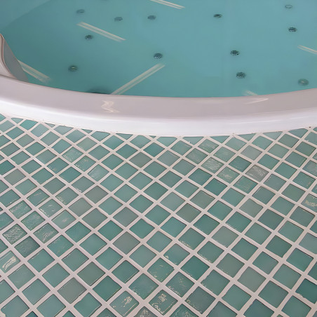 Über einem gemusterten Boden aus quadratischen, blaugrünen Glasmosaikfliesen ruht ein runder, mit Wasser gefüllter Whirlpool.