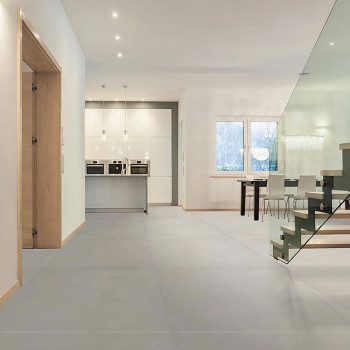 Glatte, hellgraue Bodenfliesen bedecken einen geräumigen, modernen Innenraum mit einem Küchenbereich mit weißen Schränken und ei