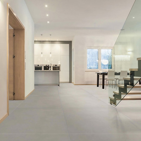 Pisos lisos em cinza claro cobrem um interior espaçoso e moderno com uma área de cozinha com armários brancos e uma escada com c