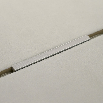 A smooth, rectangular metal handle rests across two adjacent, lightly textured cream tiles, creating a minimalist, modern aesthe