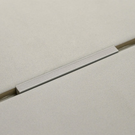 Un mango de metal liso y rectangular descansa sobre dos azulejos color crema adyacentes de textura ligera, creando una estética Un mango de metal liso y rectangular descansa sobre dos azulejos color crema adyacentes de textura ligera, creando una estética