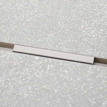 Un inserto rectangular plateado rompe el patrón uniforme de los azulejos moteados de color gris claro, formando un acento sutil 
