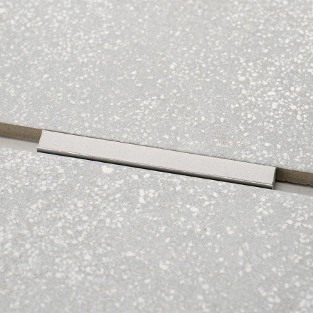 Un insert rectangulaire argenté brise le motif uniforme des carreaux gris clair mouchetés, formant un accent subtil et linéaire 