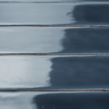 Azulejos rectangulares, brillantes y de color azul oscuro se encuentran en filas paralelas y reflejan la luz sutilmente. Crean u