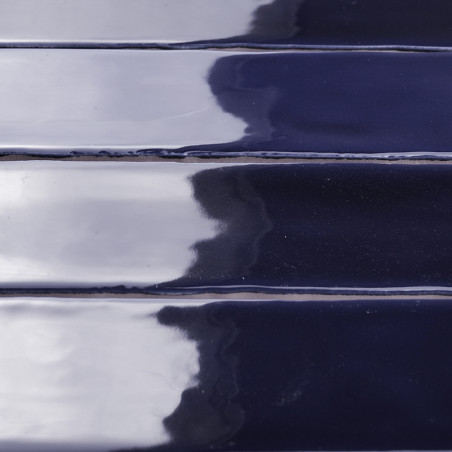 Les carreaux brillants bleu marine, alignés horizontalement, reflètent la lumière et les ombres sur leur surface selon un motif,
