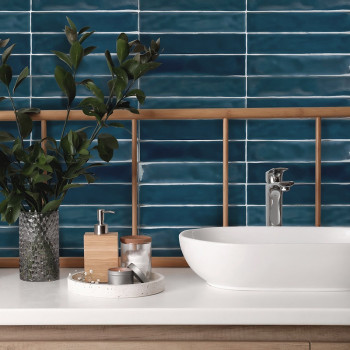 Un lavabo vasque en céramique se trouve sur un comptoir de salle de bains blanc, à côté d'une plante en pot et d'un plateau de t
