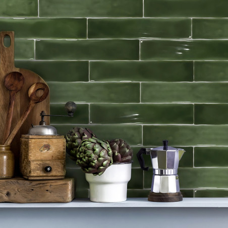 Des carreaux rectangulaires verts bordent un mur de cuisine. des ustensiles en bois, un moulin vintage, des artichauts dans une 