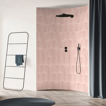 Curved wall with pink tiles holds a black showerhead and controls, surrounded by a modern bathroom with a towel rack and curtain