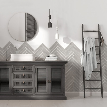 Una escena de baño presenta un mueble negro con un lavabo blanco, colocado contra una pared de azulejos en forma de espiga gris.