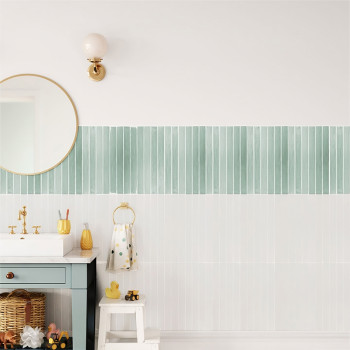 Una escena de baño presenta una pared de azulejos de color verde claro y blanco. Un espejo redondo, una lámpara, un lavabo y un 
