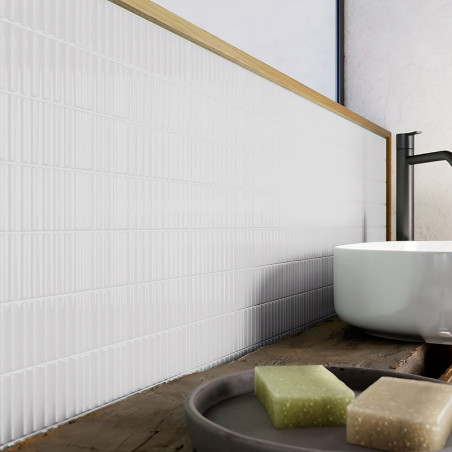 Azulejos blancos con nervaduras verticales se alinean en la pared del baño y bordean una encimera de madera. Un grifo negro se e