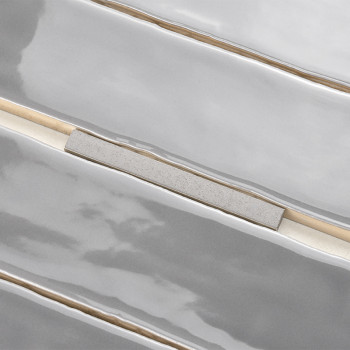 Los azulejos alargados y brillantes con un acabado gris claro están alineados horizontalmente. Tiras beige estrechas e irregular