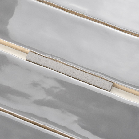 Los azulejos alargados y brillantes con un acabado gris claro están alineados horizontalmente. Tiras beige estrechas e irregular