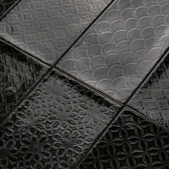 Les carreaux de céramique noire présentent des motifs géométriques complexes en relief, notamment des arcs qui se chevauchent et