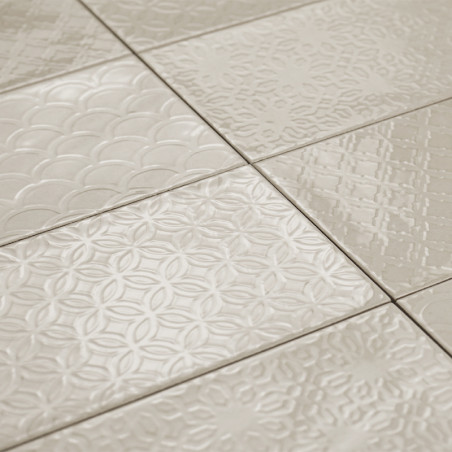 Les carreaux de céramique présentent divers motifs géométriques en relief, créant une surface texturée dans un ton beige neutre,