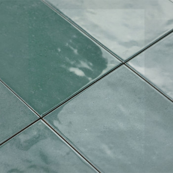 Les carreaux de céramique verte semblent brillants sous la lumière, posés selon un motif en grille. Leur surface réfléchissante 